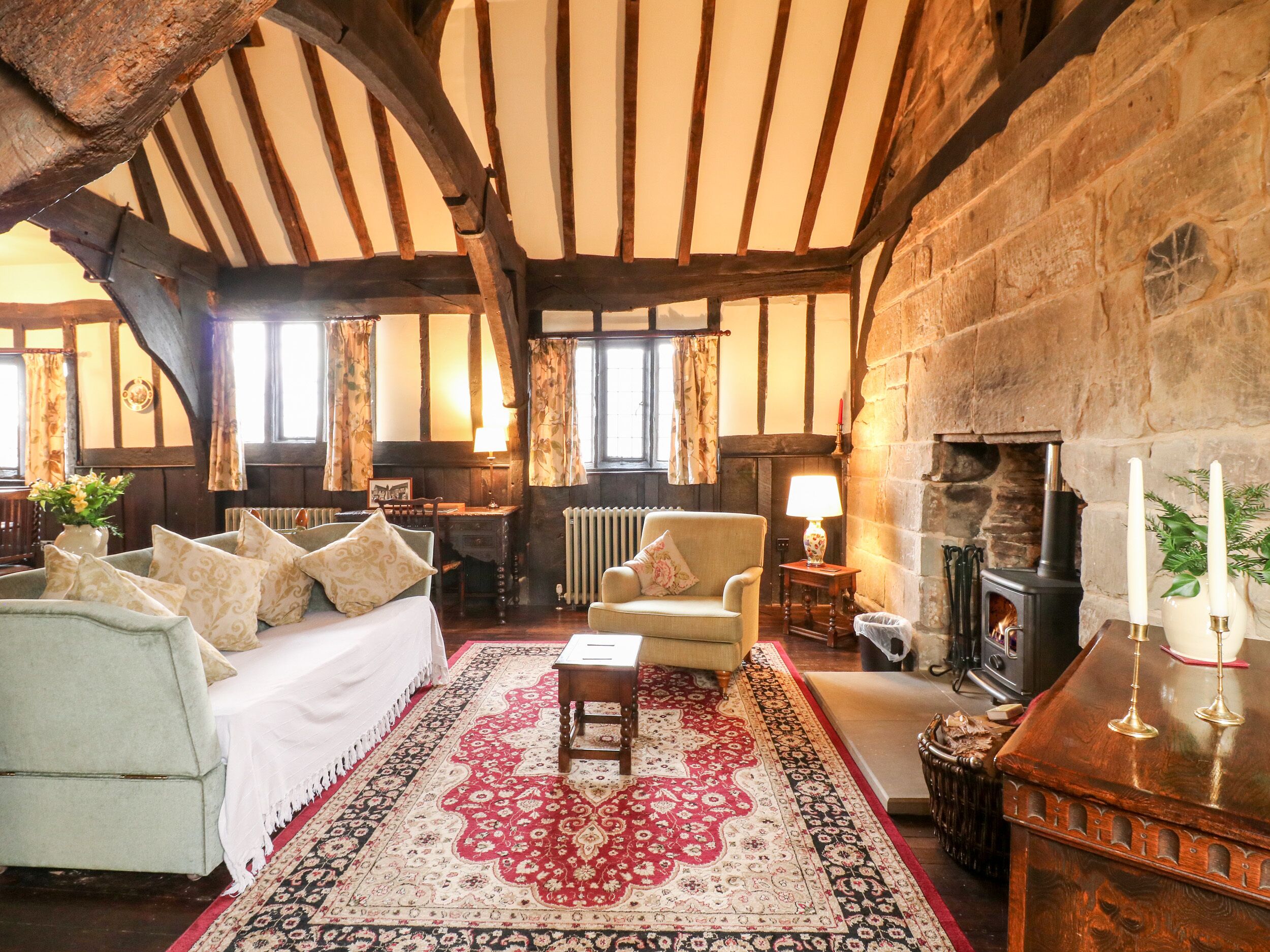 Une chambre traditionnelle avec des poutres apparentes, une cheminée, un grand tapis et un lit agrémenté de nombreux coussins.