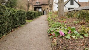 A gravel path leading to a stone building with a traditional design, surrounded by neatly trimmed hedges and flowering plants. - Porter's Lodge (Tamworth)