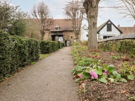 A gravel path leading to a stone building with a traditional design, surrounded by neatly trimmed hedges and flowering plants.