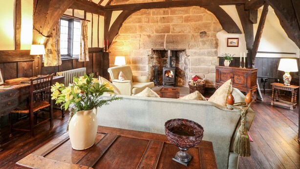 A cozy room with a stone fireplace, wooden beams, a sofa, and a table with a vase of flowers. - Porter's Lodge (Tamworth)