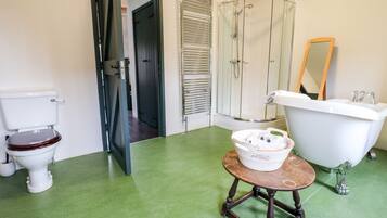 A bathroom with a toilet, a bathtub, a shower, and a small table with a basket.