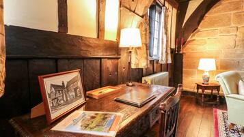 A rustic room with exposed wooden beams, a wooden table with a framed picture and a book, a chair, and a lamp.