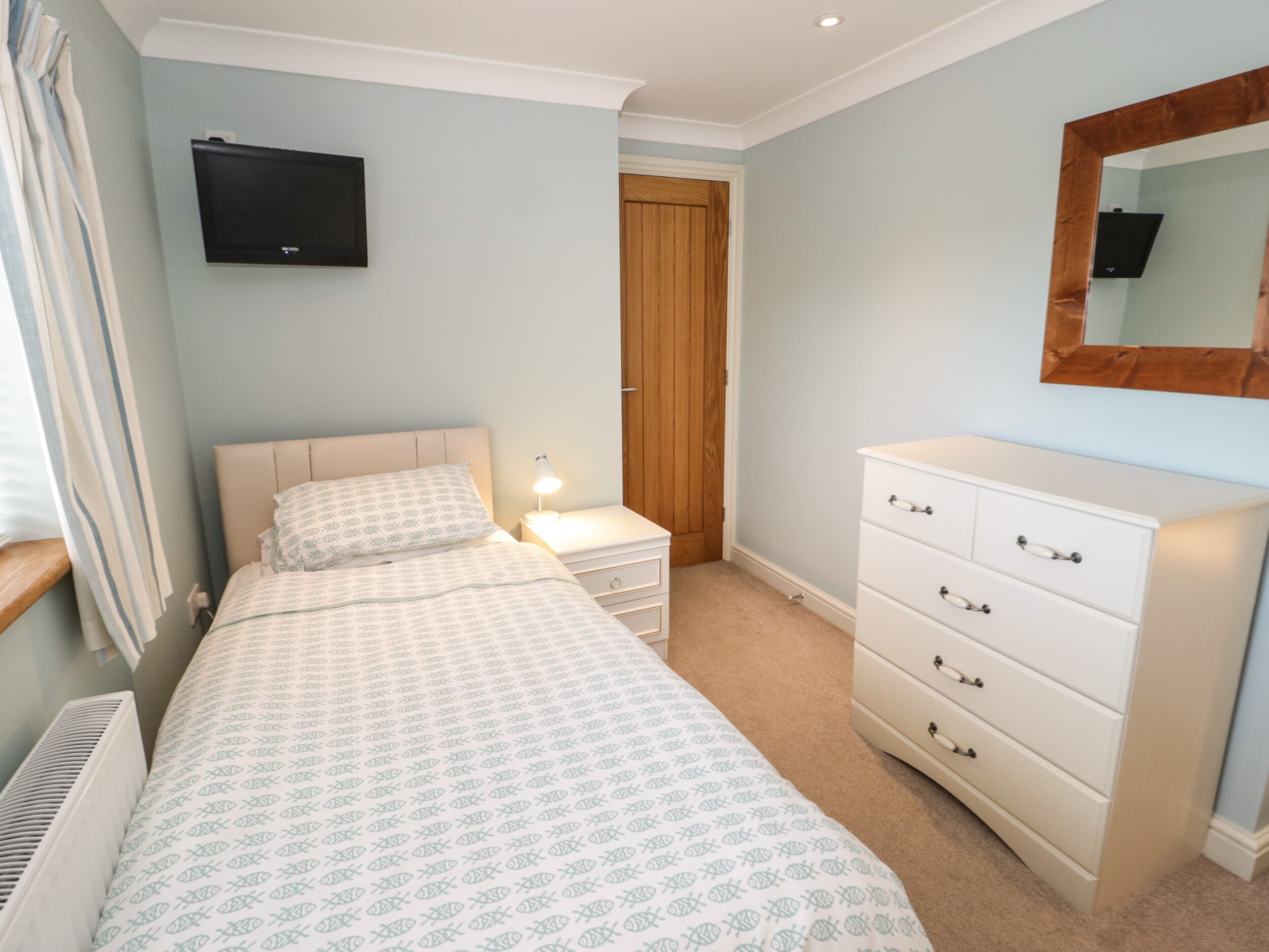 A bedroom with a bed, bedside lamp, dresser, and a TV mounted on the wall.