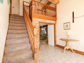 Stairs lead to a lofted area with a door to a living space featuring a sofa and a lamp.