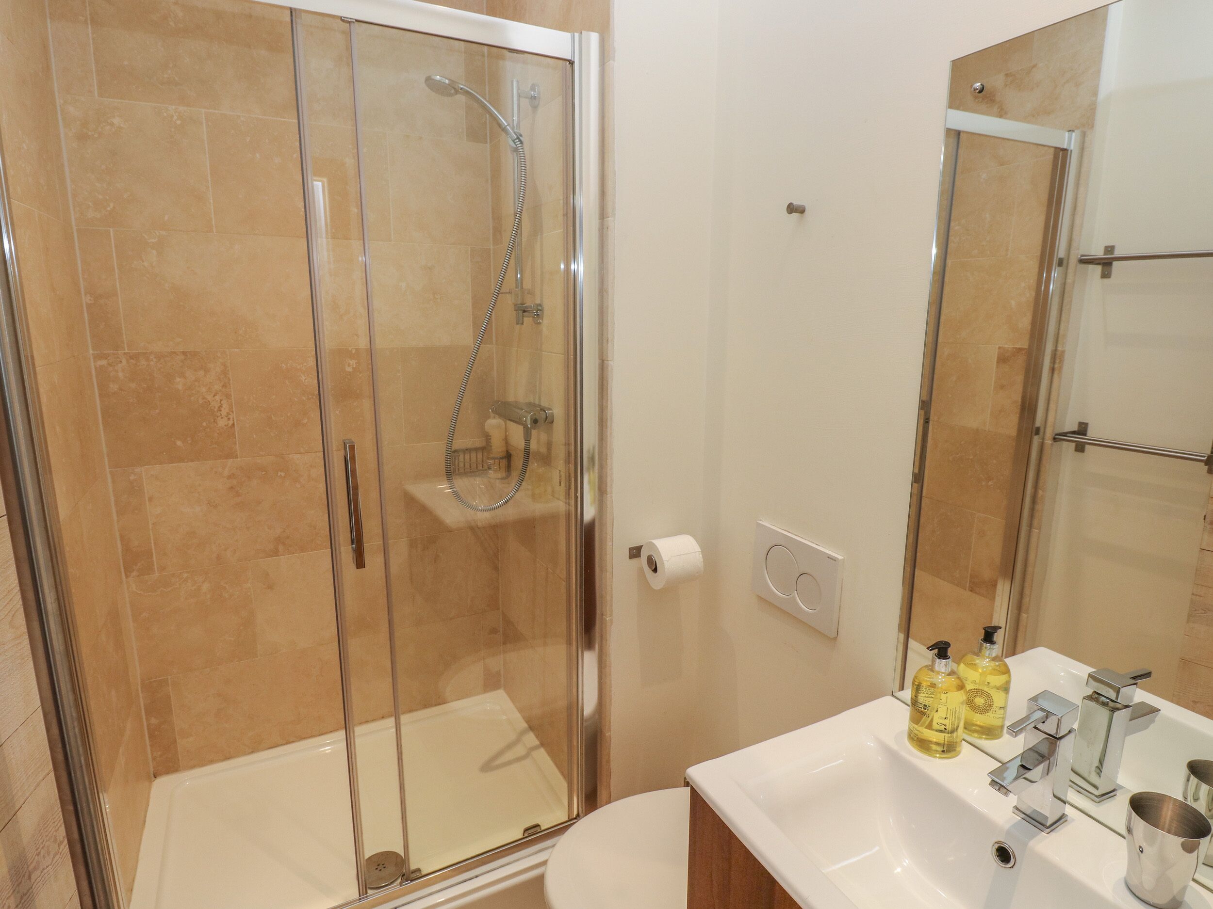 A modern bathroom with a glass-enclosed shower, a white sink with chrome fixtures, and a mirror above the sink.