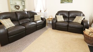 A living room with two dark brown leather sofas, a beige rug, a small wooden side table, and a painting on the wall. - Penglanowen Fawr (Aberystwyth)