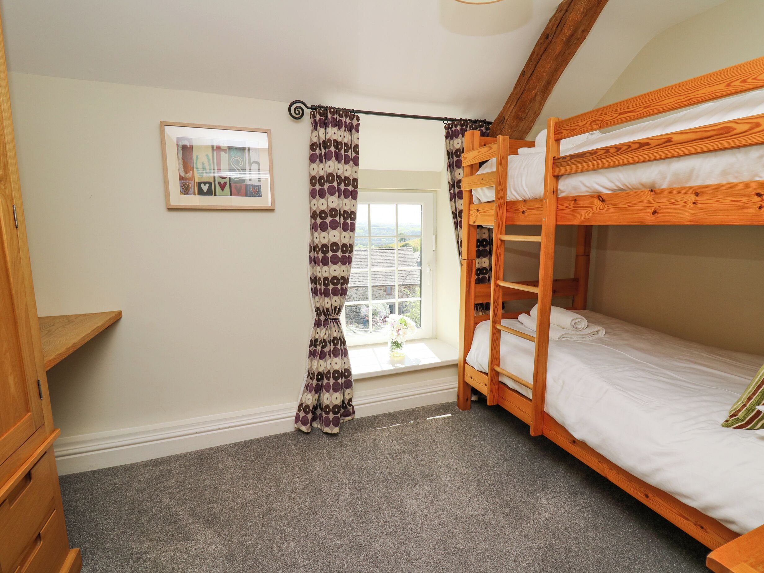 A bunk bed room with a window, curtains, a framed picture, and a wooden shelf.