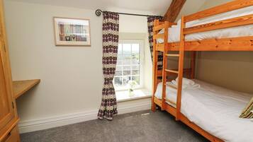 A bunk bed room with a window, curtains, a framed picture, and a wooden shelf.