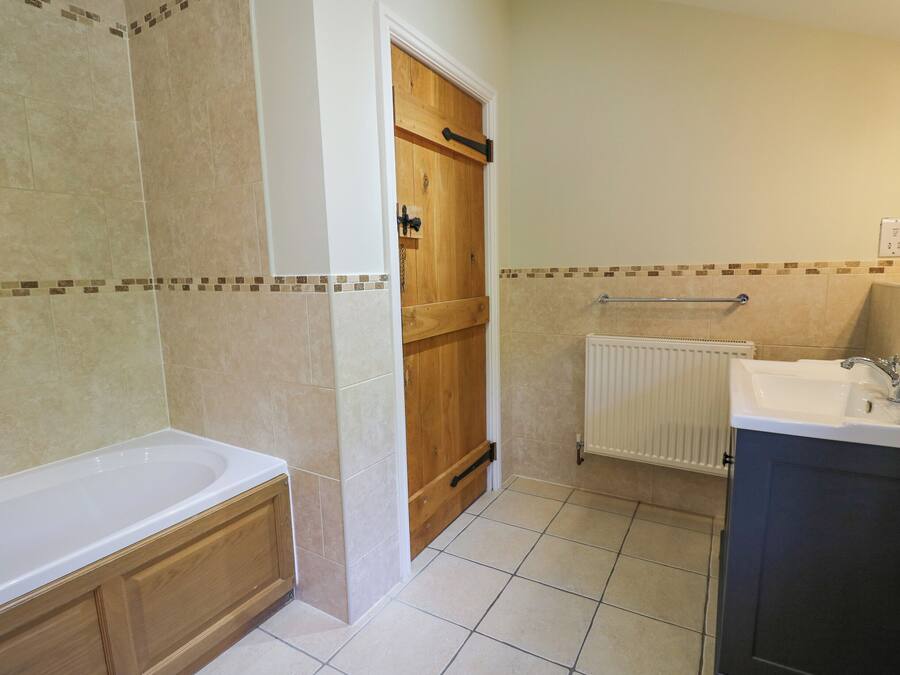 A bathroom with a bathtub, wooden door, tiled walls, and a white radiator.