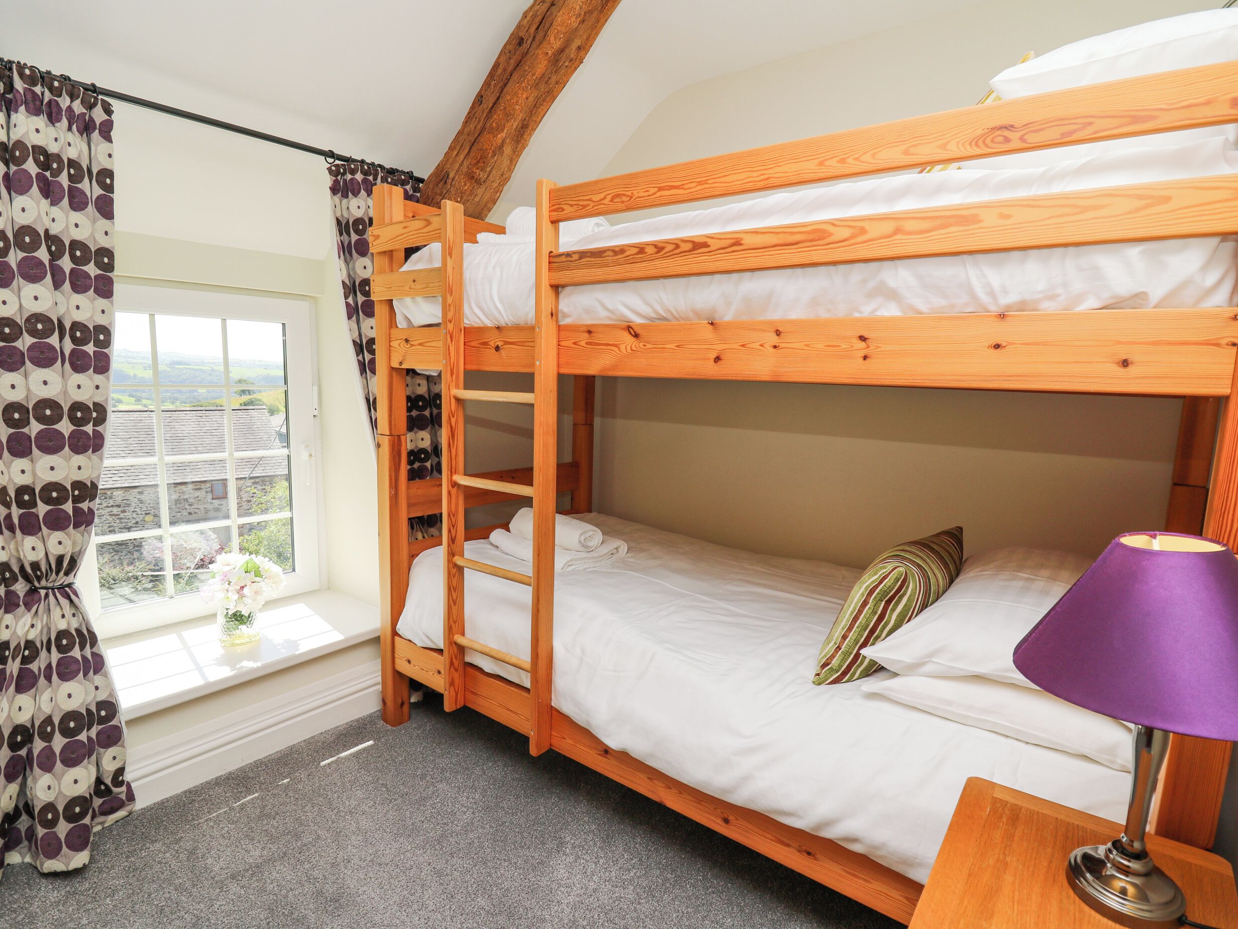 A bunk bed room with a window, curtains, and a lamp.
