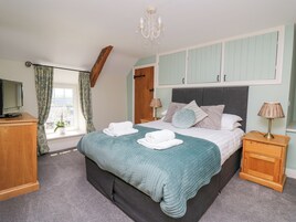 A bedroom with a bed, a television, a nightstand, a lamp, a window with curtains, and a chandelier.