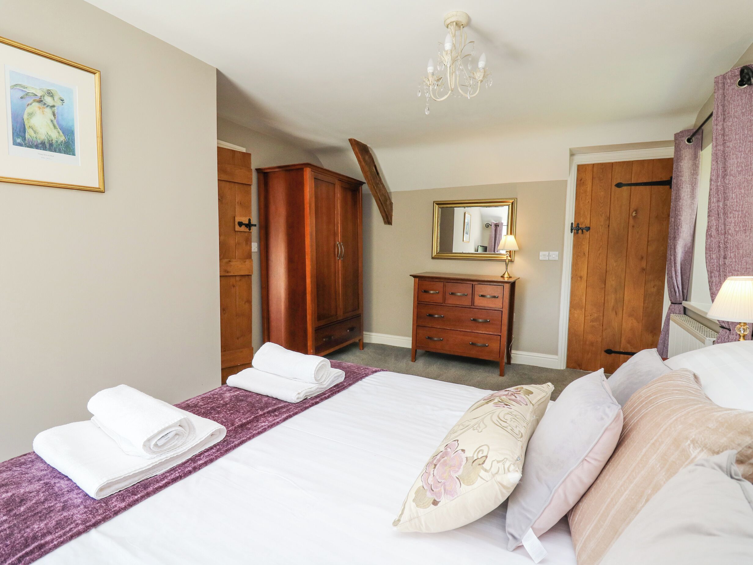 A bedroom with a bed, a dresser, a mirror, and a chandelier.