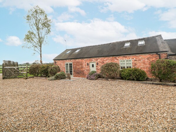 A brick building with a gravel driveway and a wooden gate. - Barnfields Holiday Cottage (Stoke-on-Trent)
