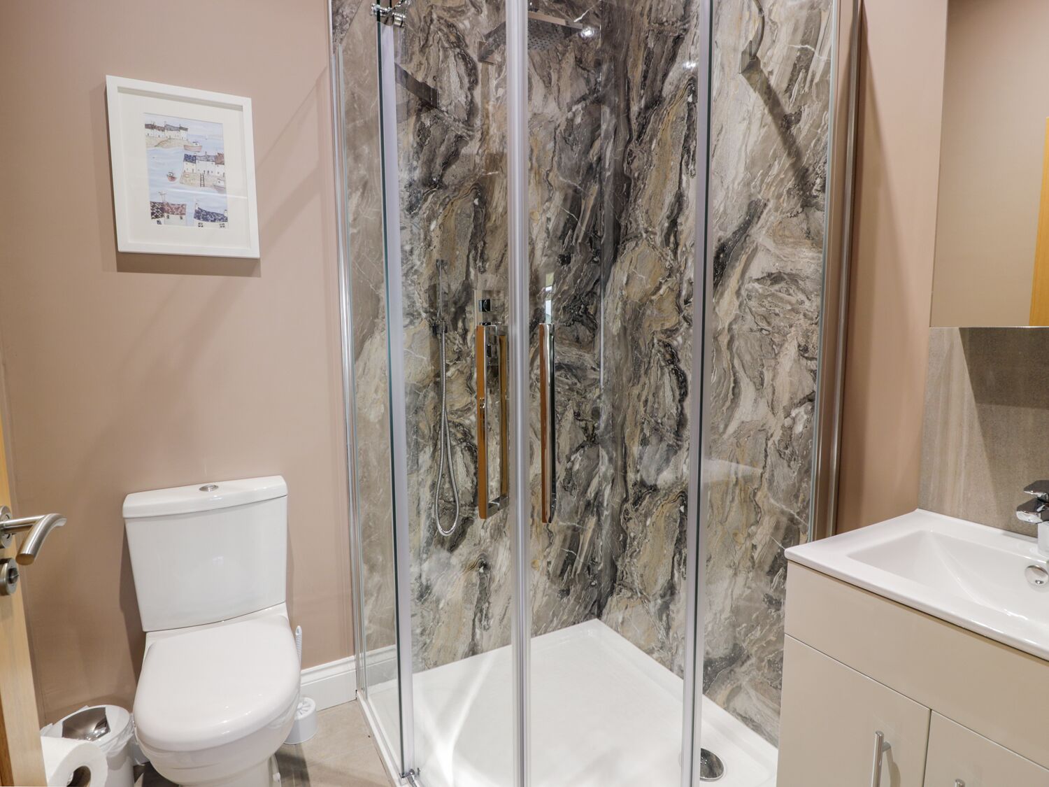 A modern bathroom with a glass-enclosed shower, a white toilet, and a sink with a marble countertop.