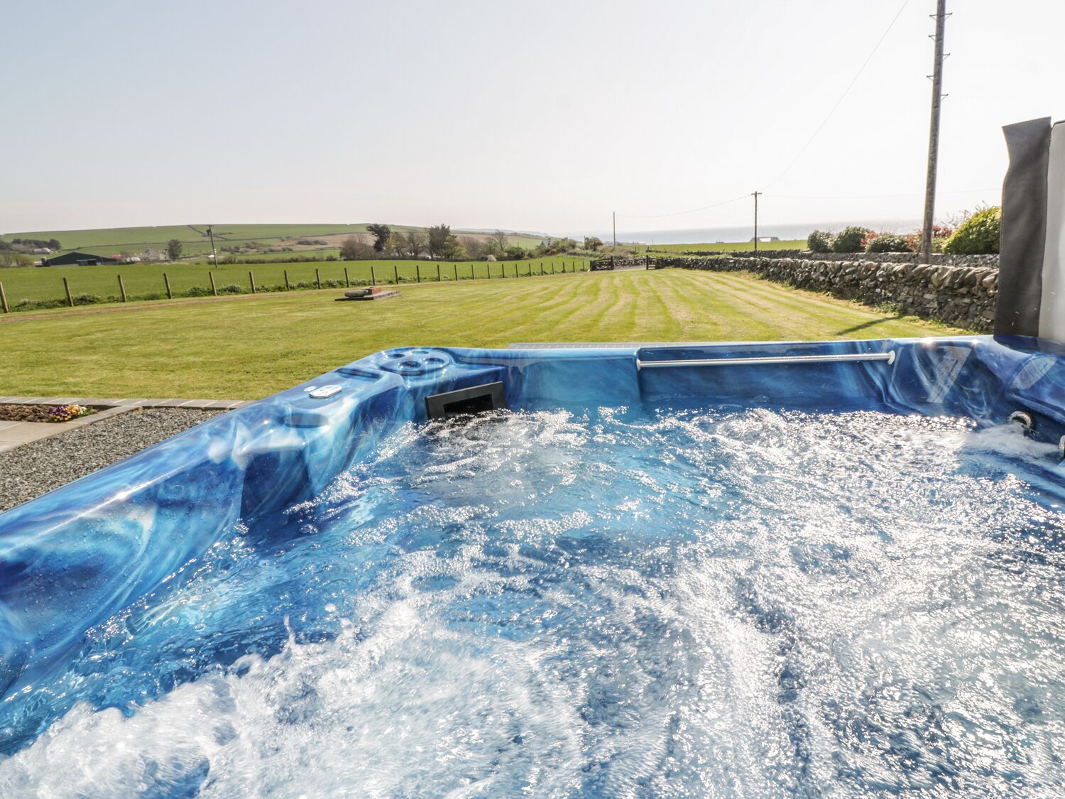 A hot tub with a view of a grassy field and stone wall.