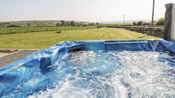 A hot tub with a view of a grassy field and stone wall.