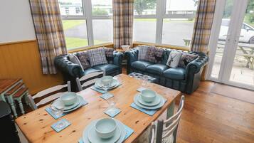 A cozy room with a wooden dining table set for four, a blue leather sofa, and a view of a parking lot through large windows.