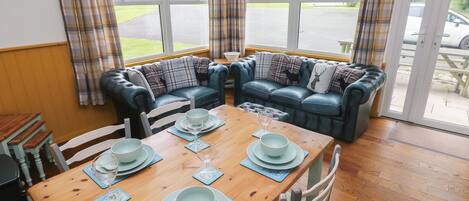 A cozy room with a wooden dining table set for four, a blue leather sofa, and a view of a parking lot through large windows.