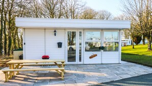 A small white building with a wooden bench and a grill outside.