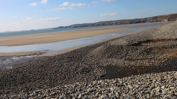A pebbly beach with a wide sandy shore and distant cliffs.
