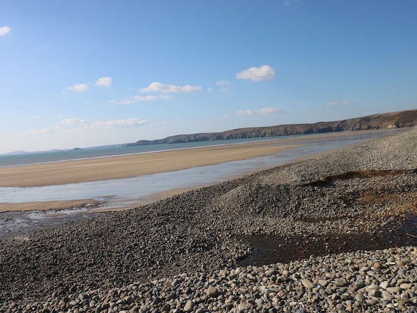 A pebbly beach with a wide sandy shore and distant cliffs. - Driftwood (Haverfordwest)