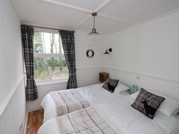 Een slaapkamer met twee bedden, een raam met gordijnen, een hanglamp en een klein nachtkastje met een lamp.