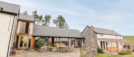 A stone building with a covered patio area, wooden furniture, and a stone pathway leading to the entrance.