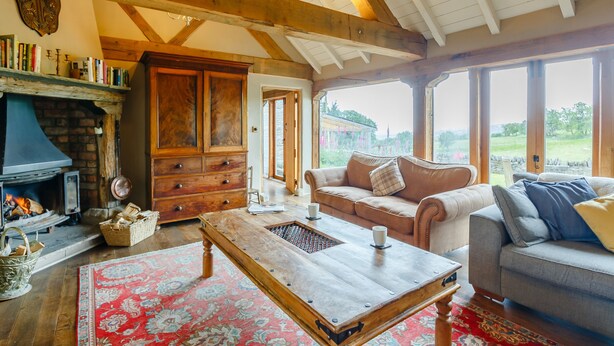 A cozy living room with a fireplace, wooden beams, a sofa, and a coffee table. - Pant Dafydd Goch (Llangollen)