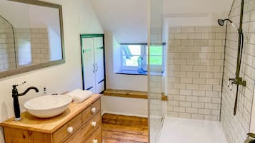 Un baño moderno con tocador de madera, un espejo grande, un lavabo blanco y una zona de ducha con mampara de cristal.