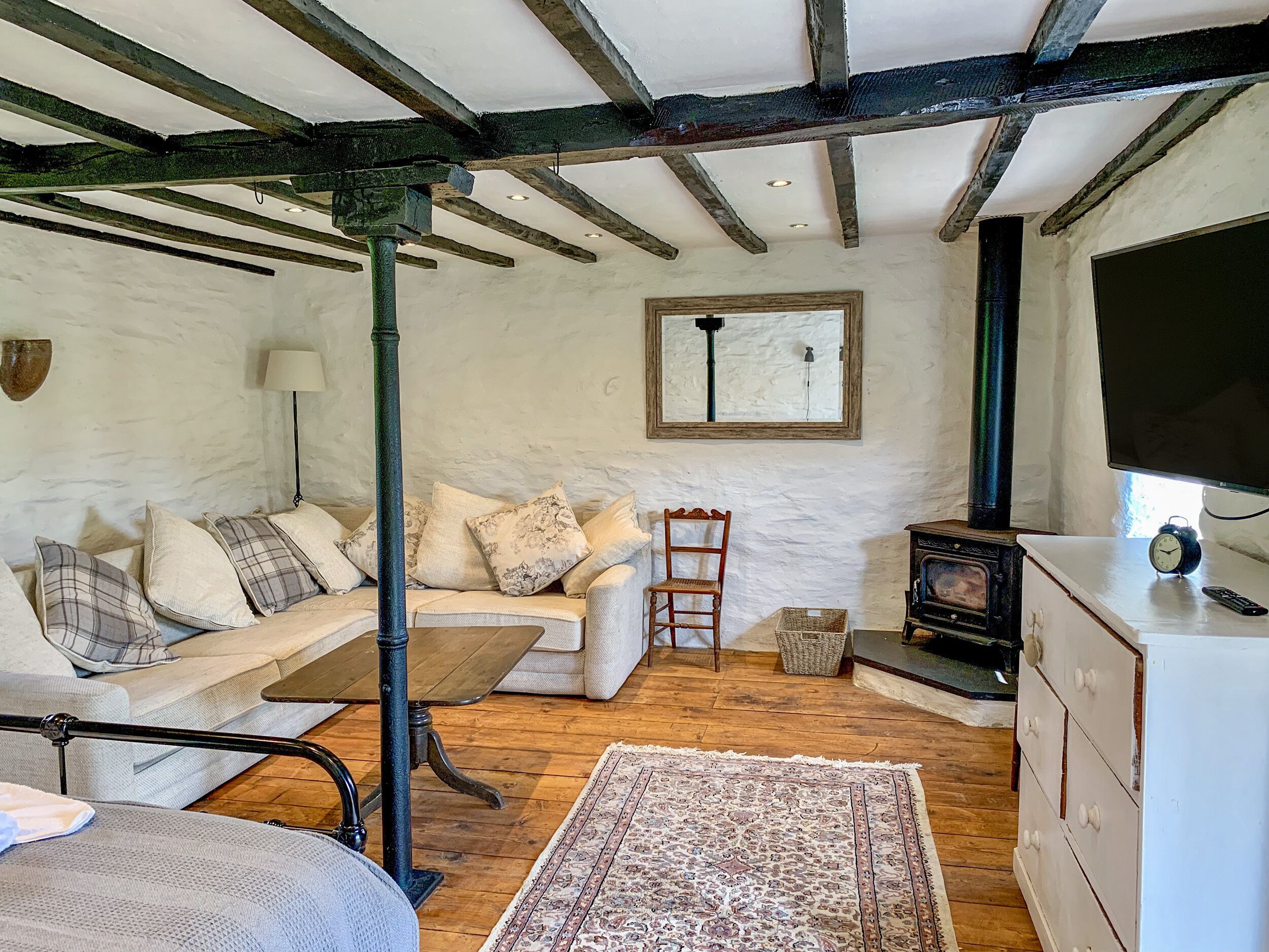A cozy room with a wooden ceiling, a sofa with patterned cushions, a wooden chair, a small table, a rug, a television, and a fireplace.