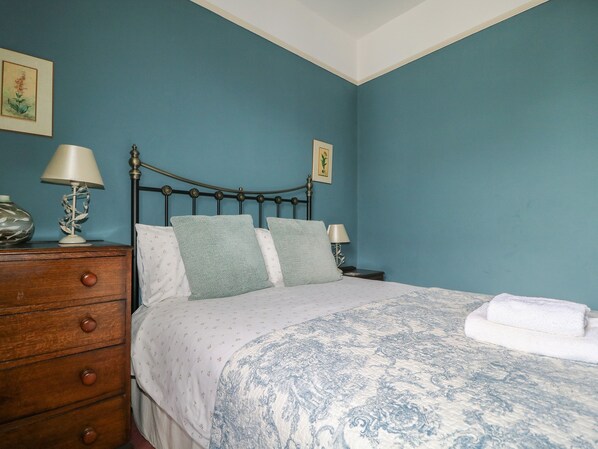 A bedroom with a bed, a wooden dresser, two bedside tables with lamps, and two framed pictures on the wall.