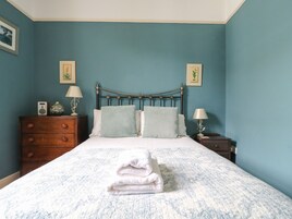 Un dormitorio con una cama, dos mesitas de noche, un aparador y dos lámparas de pared.