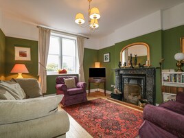Una sala de estar con chimenea, paredes verdes, un ventanal con cortinas, un sofá, un sillón y una estantería.