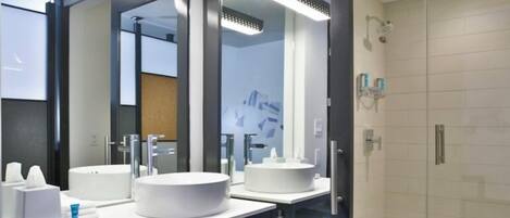 A modern bathroom with two round white sinks, a glass shower enclosure, and a toilet.