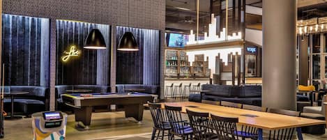 A modern lounge area with a pool table, seating, and a bar.