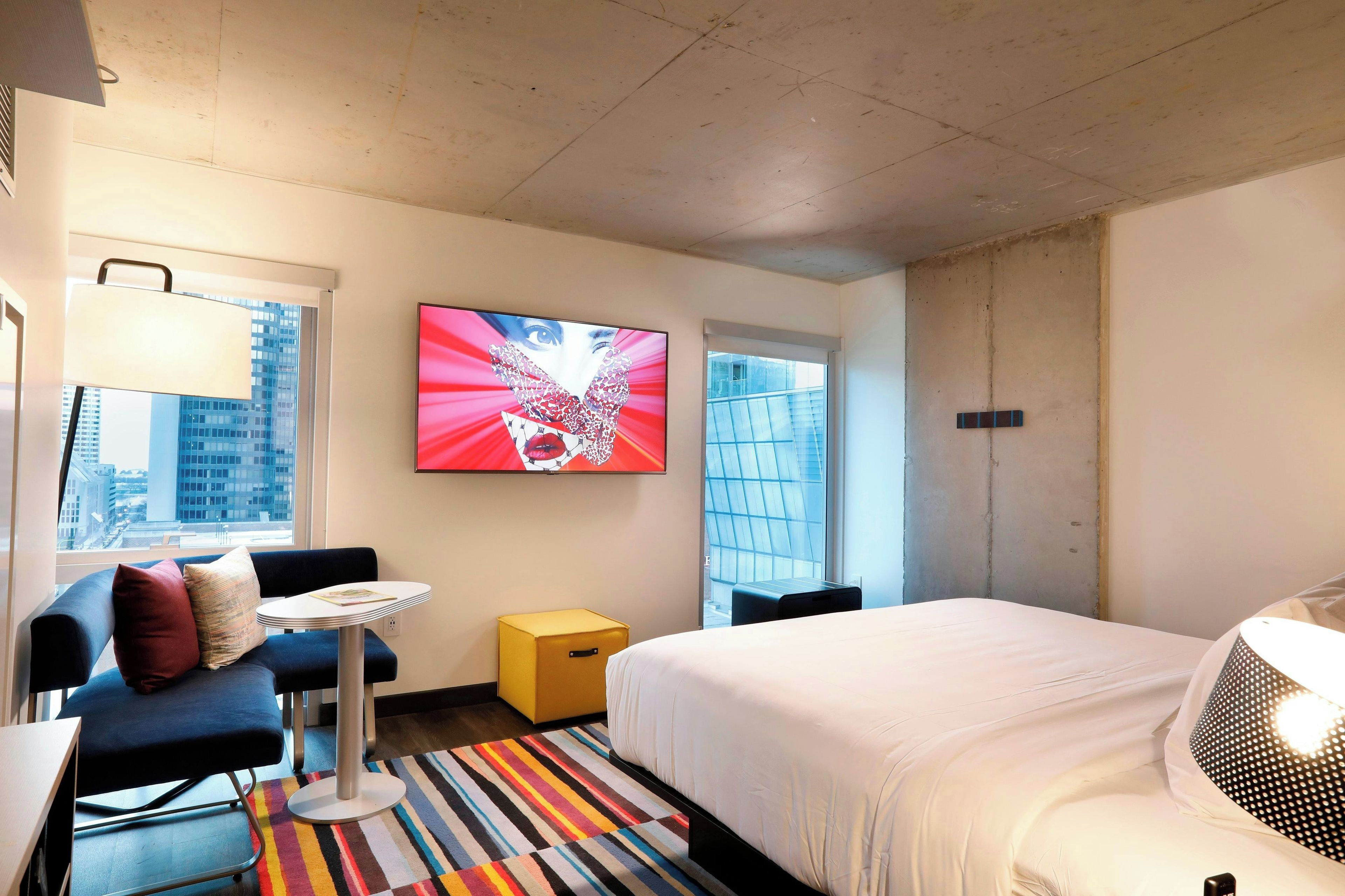 A hotel room with a bed, a desk, a chair, a TV, and a window with a city view.