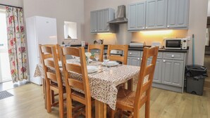 Comedor con una mesa lista para cuatro, sillas de madera y una cocina al fondo con armarios grises y un microondas.
