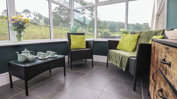 Un invernadero con mobiliario de mimbre, una mesa con teteras y vistas a la vegetación.
