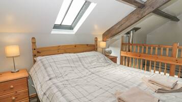 A bedroom with a sloped ceiling, a skylight, a wooden headboard, a bed with a plaid bedspread, a nightstand with a lamp, and a wooden dresser.