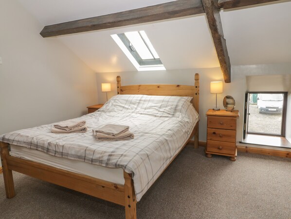 Quarto com cama de madeira, claraboia, mesa de cabeceira com luminária e vista para um veículo pela janela.