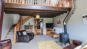 A spacious living area with a high wooden staircase, a leather sofa, a wooden table, a television, and a wood-burning stove. - Hayloft (Scarborough)