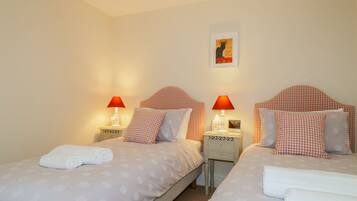 Een tweepersoonskamer met twee bedden, elk met een rode geruit hoofdbord, wit beddengoed en een rode bureaulamp.