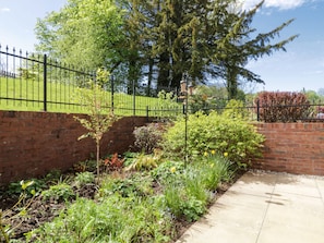 Stroll through the serene garden, surrounded by vibrant flowers and lush greenery, along a paved pathway leading to a charming entrance.
