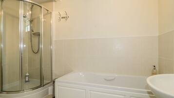 A bathroom with a glass-enclosed shower, a white bathtub, and a sink.
