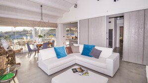 Ein modernes Wohnzimmer mit einem weißen Ecksofa, einem Glastisch und einem Essbereich mit Tisch und Stühlen.