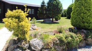 A lodge with a stone facade, a well-maintained lawn, and a variety of trees and shrubs. - Cedar Lodge (Bodmin)