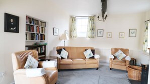 A living room with a beige sofa set, a bookshelf, and a chandelier.