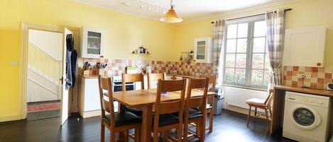 Una cocina con una mesa de comedor, sillas, una lavadora y un ventanal con cortinas.