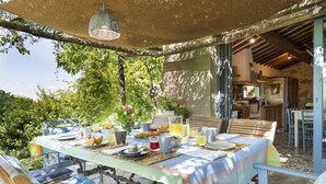 Un espacio exterior para comer con una mesa dispuesta para el desayuno, rodeada de sillas y cubierta por un toldo.