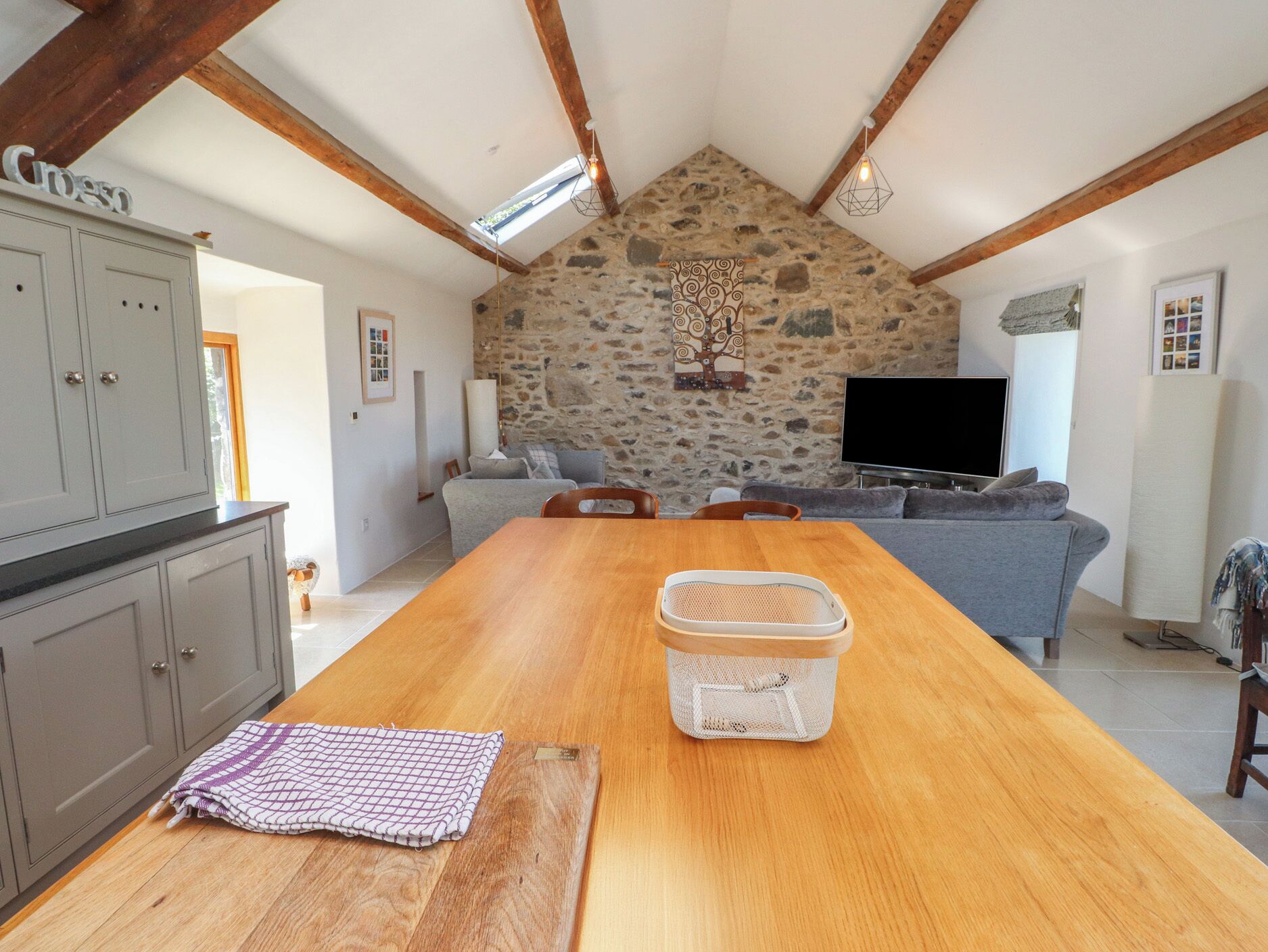A spacious living area with a long wooden table, stone wall, and a television.